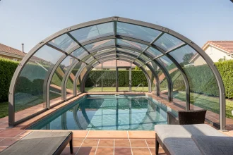 Abri de piscine en polycarbonate rétractable protégeant l'eau turquoise d'une piscine extérieure dans un jardin entretenu